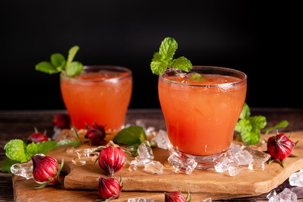 Iced Roselle Teeglas mit frischen Rosellefrüchten auf Holztisch für ein gesundes Kräutergetränkkonzept. Kräuter-Bio-Tee für gute Gesundheit.