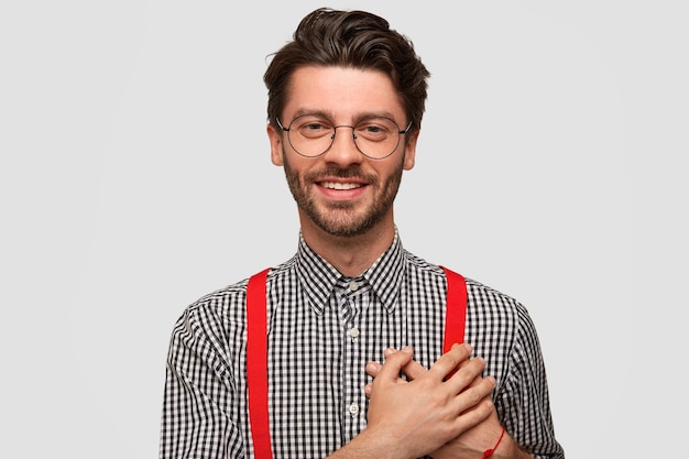 Kostenloses Foto ich bin dir so dankbar! attraktiver, freundlich aussehender hipster mit trendigem haarschnitt, der beide handflächen im herzen hält