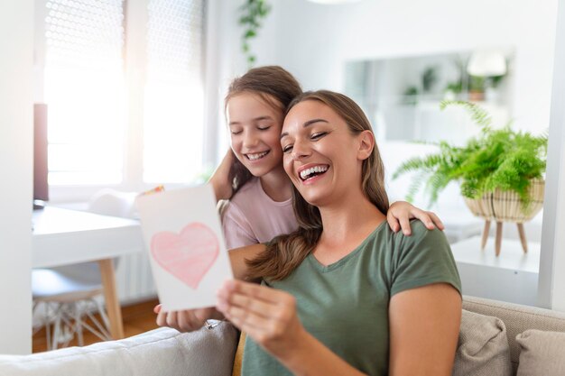 Ich liebe meine Mama Attraktive junge Frau mit kleinen süßen Mädchen verbringt Zeit zusammen zu Hause und dankt für handgemachte Karte mit Liebessymbol und Blumen Glückliches Familienkonzept Muttertag