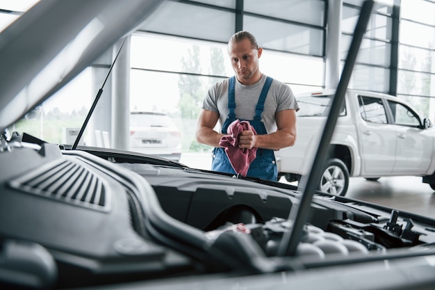 Ich muss genauer hinsehen. Mann in blauer Uniform arbeitet mit kaputtem Auto. Reparaturen durchführen