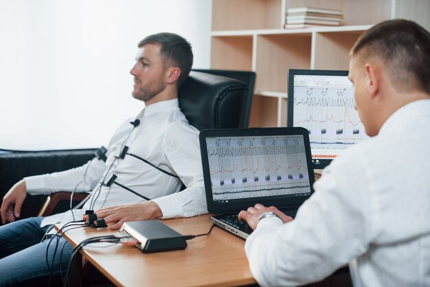 Ich war nicht da Verdächtiger Mann übergibt Lügendetektor im Büro. Fragen stellen. Polygraphentest