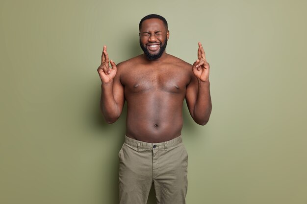 Ich will gewinnen. Positiver dunkelhäutiger Afroamerikaner drückt die Daumen und wünscht sich bessere Posen mit nacktem Oberkörper