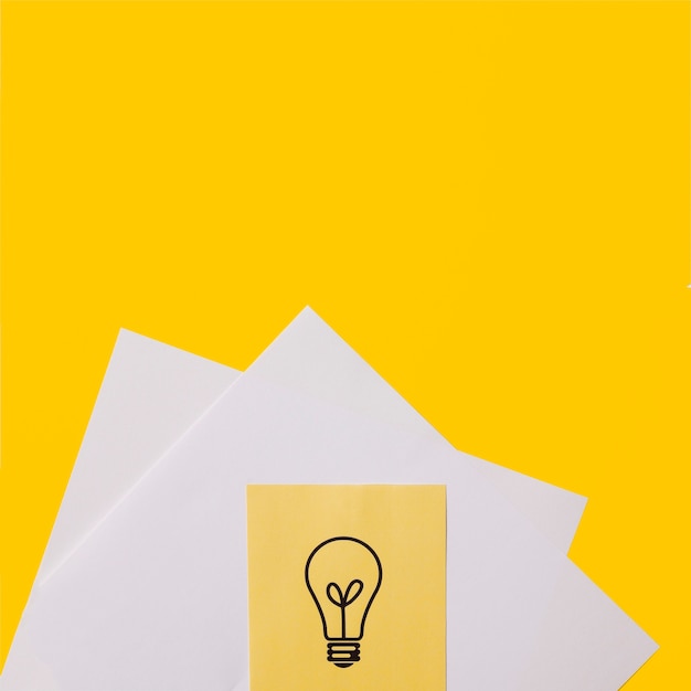 Ideenbirnenikone auf klebriger Anmerkung über Weißbuch gegen gelben Hintergrund