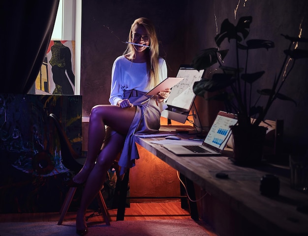 Im gemütlichen dunklen Loft sitzt eine attraktive Studentin beim Lernen auf dem Tisch.