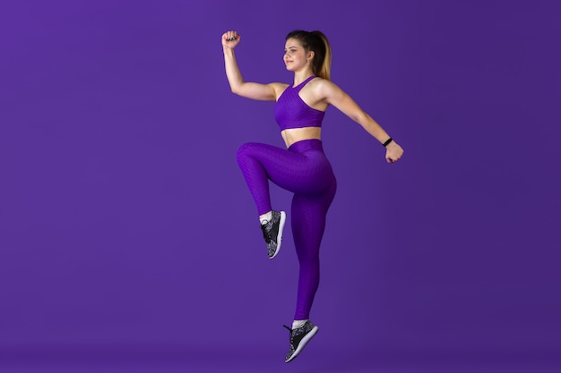 Im Sprung. Schöne junge Sportlerin, die in einfarbigem purpurrotem Porträt übt. Sportliches kaukasisches Fit-Modelltraining. Bodybuilding, gesunder Lebensstil, Schönheits- und Aktionskonzept.