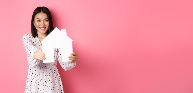Immobilien erwachsene asiatische Frau auf der Suche nach Hausmodell und lächelnder Promo von Broker com