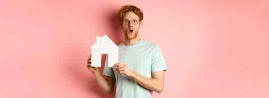 Kostenloses Foto immobilien überraschten jungen mann mit roten haaren und bart, der eine brille und ein t-shirt mit papier-hou trug