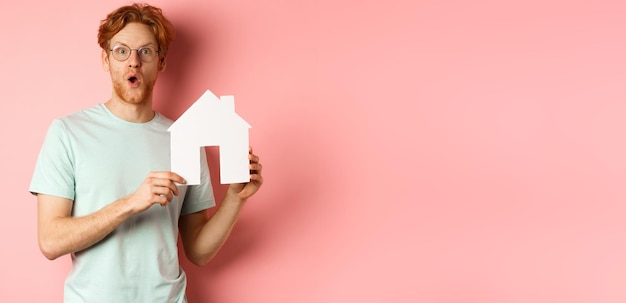 Kostenloses Foto immobilien überraschten jungen mann mit roten haaren und bart, der eine brille und ein t-shirt mit papier-hou trug