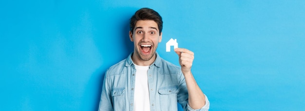Immobilienkonzept glücklicher junger Mann, der aufgeregt aussieht, fand Wohnung mit kleinem Hausmodell standi