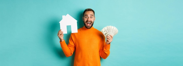 Kostenloses Foto immobilienkonzept und hypothekenkonzept aufgeregter mann, der dollar und papiermarkt des hauskaufs zeigt