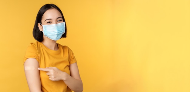 Impf- und covid-pandemiekonzept lächelnde asiatin in medizinischer gesichtsmaske, die ihre schulter zeigt