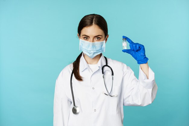 Impfkampagne lächelnde Ärztin mit medizinischer Gesichtsmaske und Handschuhen, die einen Impfstoff gegen Covid zeigen