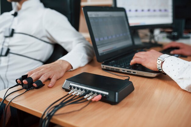 In Arbeit. Verdächtiger Mann übergibt Lügendetektor im Büro. Fragen stellen. Polygraphentest