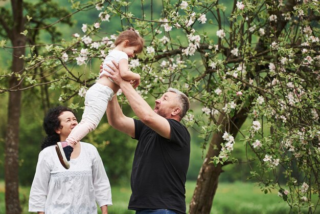 In den Händen des Großvaters. Fröhliches Paar genießt schönes Wochenende im Freien mit Enkelin. Gutes Frühlingswetter