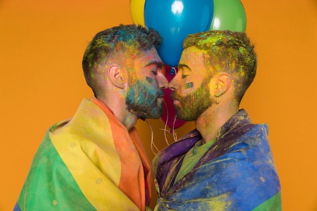 Kostenloses Foto in den homosexuellen paaren der farbe wurde das küssen eingewickelt, das in der regenbogenflagge eingewickelt wurde