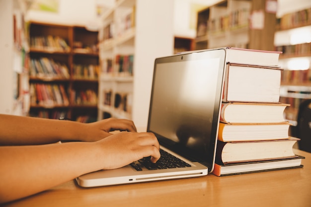 In der Bibliothek - Junge Studentin, die ihren Laptop in einer Bibliothek verwendet