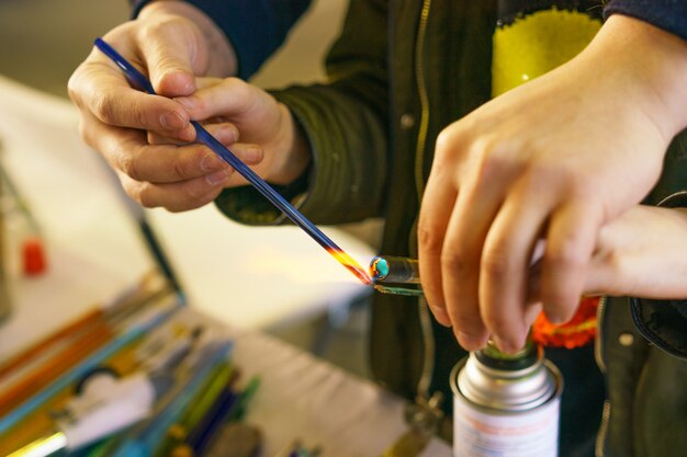 In der Meisterklasse über die Herstellung von dekorativem Spielzeug aus Glas zeigt der Lehrer, wie man schmilzt und macht. Nahaufnahme und Weichzeichner