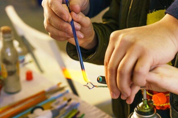 In der Meisterklasse über die Herstellung von dekorativem Spielzeug aus Glas zeigt der Lehrer, wie man schmilzt und macht. Nahaufnahme und Weichzeichner