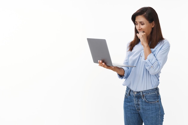 In Panik geratene Frau, die nervös in die Faust beißt, hält den Laptop-Bildschirm ängstlich und hat ängstlich einen Computervirus, der wichtige Arbeitsdokumente löscht, die besorgten und verzweifelten weißen Hintergrund darstellen