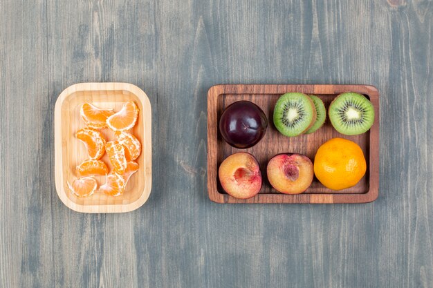 In Scheiben geschnittene frische Kiwi mit Orange und Pflaume auf einem Holzbrett