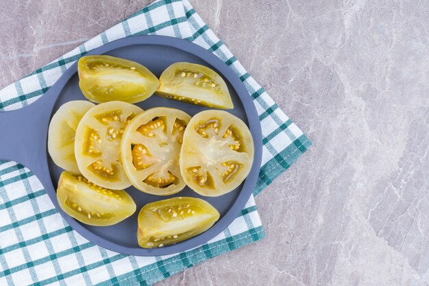 In Scheiben geschnittene konservierte Tomaten auf einer Holzpfanne auf einem Geschirrtuch auf dem Marmor.