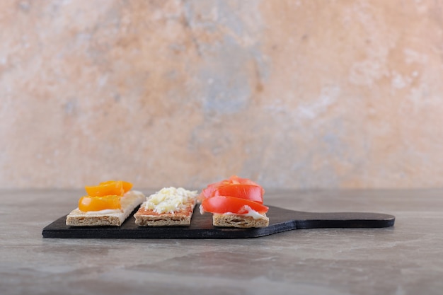 In Scheiben geschnittene reife und unreife Tomaten auf knusprigem Brot auf dem Schneidebrett, auf der Marmoroberfläche