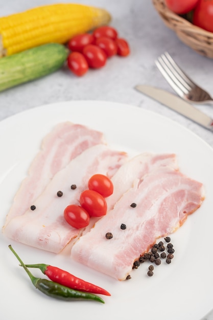 In Scheiben geschnittener Schweinebauch auf einem weißen Teller mit Pfeffersamen und Tomaten.