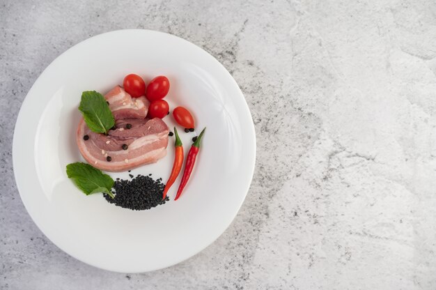 In Scheiben geschnittener Schweinebauch auf einem weißen Teller mit Pfeffersamen und Tomaten.