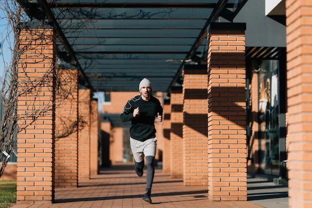 In voller Länge vom entschlossenen athletischen Mann, der in die Stadt läuft