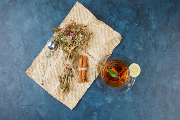 In Zeitungspapier gewickelte Blumen mit einer Tasse Tee, Zimt und einem Teesieb