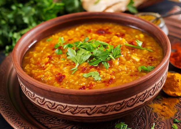 Indian Dhal würziges Curry in Schüssel, Gewürzen, Kräutern, rustikalem schwarzem Holztisch.