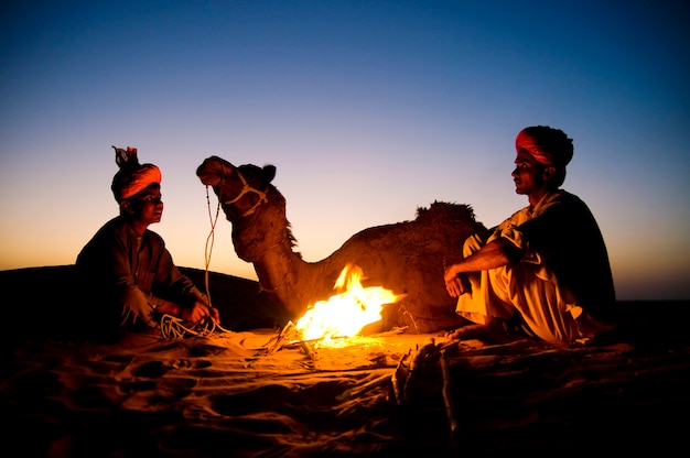 Kostenloses Foto indische männer, die durch das feuer mit ihrem kamel stillstehen