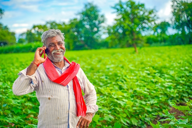 Indischer landwirt, der auf handy am landwirtschaftsfeld spricht