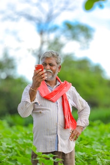 Indischer landwirt, der handy am landwirtschaftsfeld verwendet