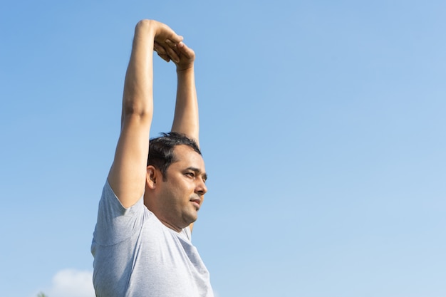 Indischer Mann, der draußen Arme mit blauem Himmel im Hintergrund ausdehnt. Yoga-Konzept.
