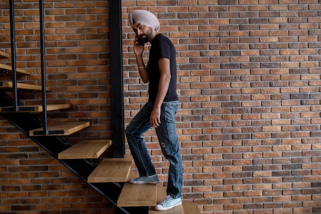 Indischer Mann mit beigem Turban, der auf der Treppe steht und telefoniert