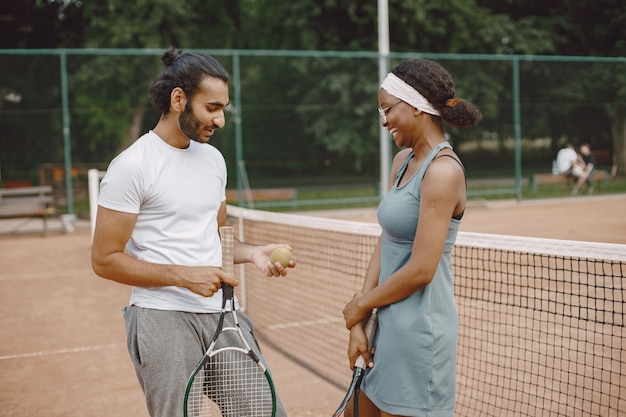 Indischer Mann und schwarze Amerikanerin stehen auf einem Tennisplatz