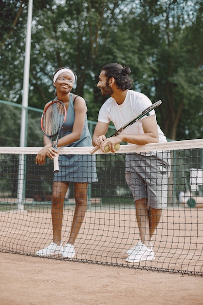 Indischer Mann und schwarze Amerikanerin stehen auf einem Tennisplatz