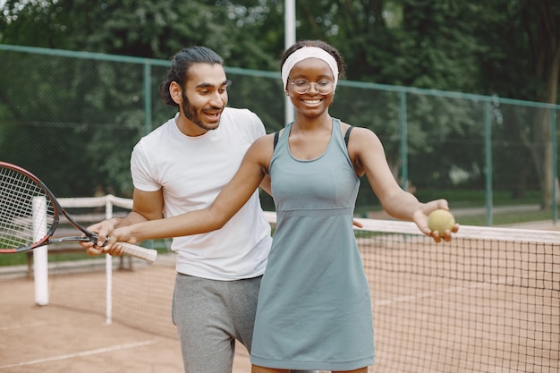 Indischer Mann und schwarze Amerikanerin stehen auf einem Tennisplatz