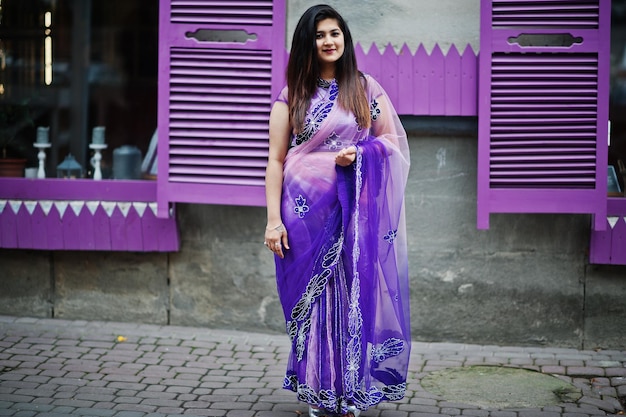 Indisches hinduistisches Mädchen im traditionellen violetten Saree posierte auf der Straße vor lila Fenstern