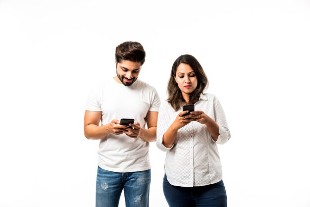 Indisches junges paar mit smartphone oder handy, isoliert auf weißem hintergrund oder vor rotem backsteinhintergrund