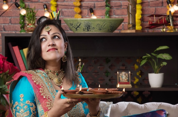 Indisches mädchen, das diwali diya in traditioneller kleidung hält, auf ein selfie-bild klickt oder über das smartphone spricht.