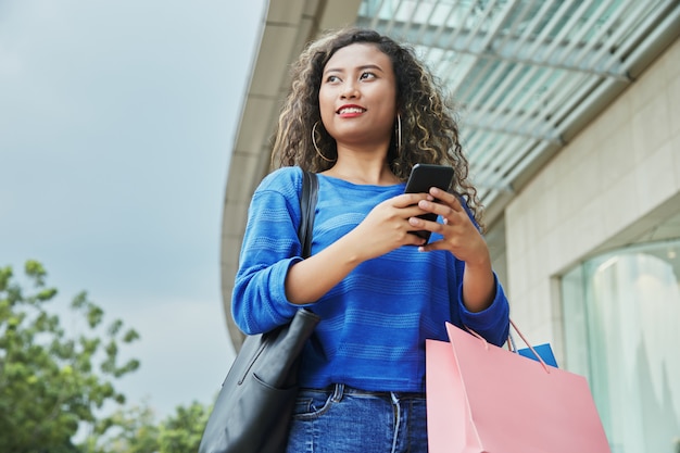 Indonesierin mit Papiertüten unter Verwendung des Smartphone