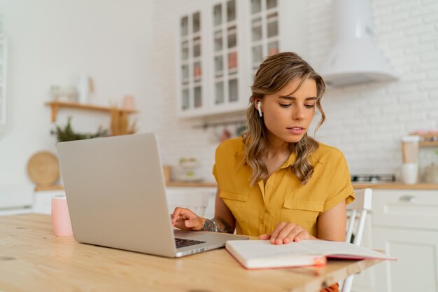 Indoor-Lifestyle-Foto einer glücklichen Hausfrau, die einige Quittungen durchsucht und Kaffee in einer hellen, modernen Küche trinkt