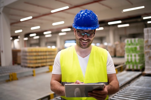 Industriearbeiter in der reflektierenden Jacke und im Helm, die Tablette im modernen Fabrikinnenraum betrachten