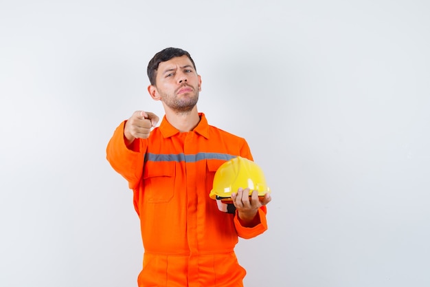 Industriemann, der Helm hält, in Uniform zeigt und selbstbewusst aussieht, Vorderansicht.