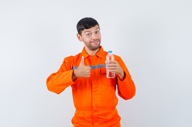 Industriemann in der Uniform, die Flasche Wasser hält, zeigt Daumen hoch und schaut fröhlich, Vorderansicht.