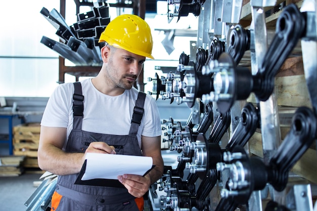 Industriemitarbeiter, der Uniform und gelben Helm trägt, der Produktion in Fabrik prüft