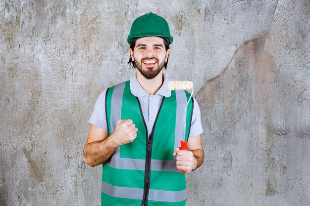 Ingenieur in gelber Ausrüstung und Helm, der eine Trimmrolle hält und ein positives Handzeichen zeigt