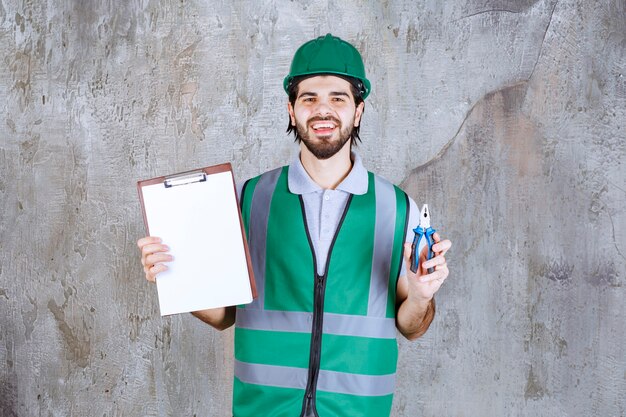 Ingenieur in gelber Ausrüstung und Helm mit Zangen und einer leeren Aufgabenliste.